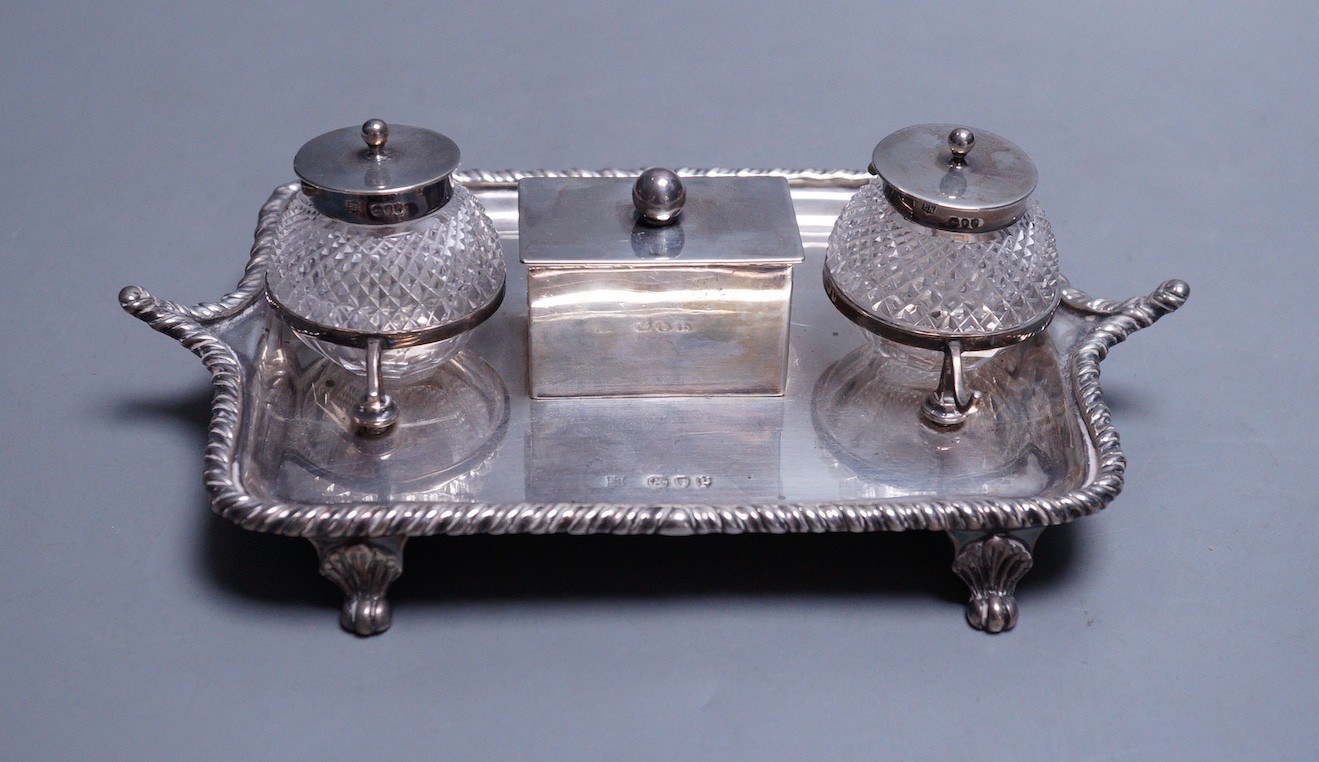 A late Victorian silver inkstand, with two mounted glass wells and central lidded compartment, Edward Hutton, London, 1890, 19cm, gross 9oz.